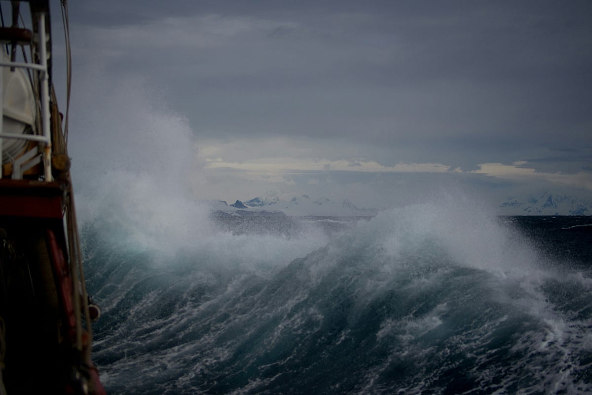 Rough ocean waves seen from a ship's railing under a stormy gray sky.