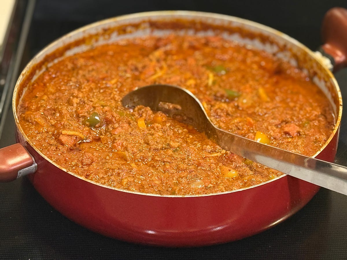 A pot of chili with a spoon resting inside it.